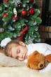 Little girl sleeping with teddy bear near christmas tree