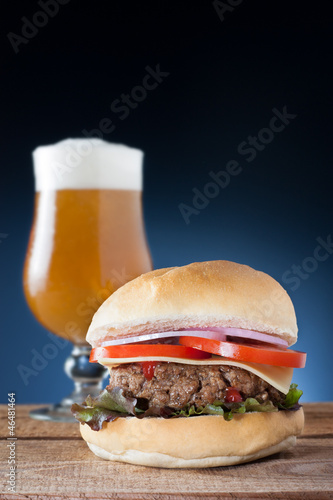 Photo: Burger with cheese, onion, tomato and lettuce served with a beer Burger with cheese, onion, tomato and lettuce served with a beer