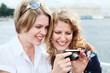Photo: Two happy women looking at screen of simple hand-held camera Two happy women looking at screen of simple hand-held camera