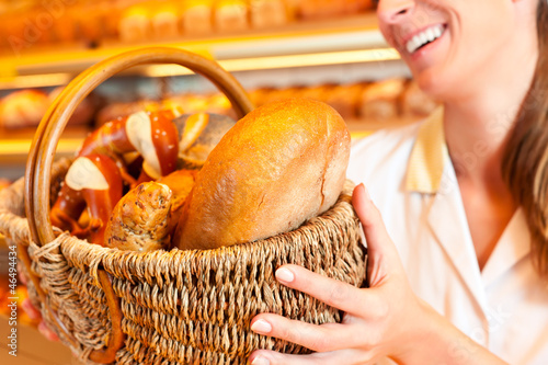 Photo: Female baker selling bread by basket in bakery Female baker selling bread by basket in bakery