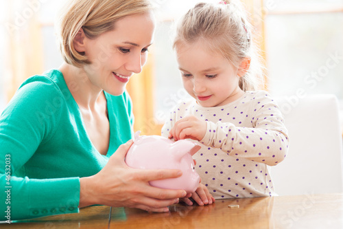 Photo: Mother and daughter putting coins into piggy bank Mother and daughter putting coins into piggy bank
