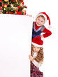 Children in Santa hat with banner near Christmas tree.