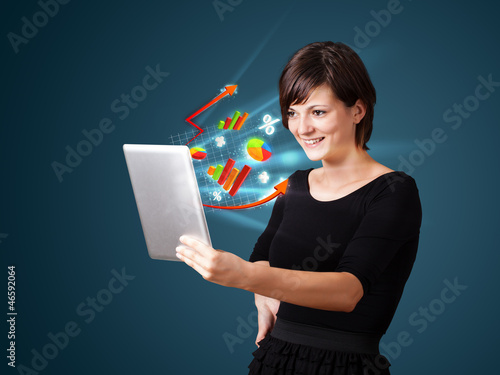 Photo: Young woman looking at modern tablet with abstract lights and va Young woman looking at modern tablet with abstract lights and va