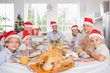 Happy family wearing santa hats around the dinner table