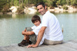 a father and his son seated on a pontoon faces a lake