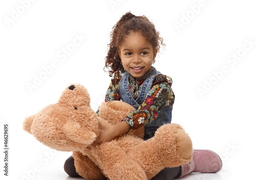 Photo: Cute ethnic girl playing with plush bear smiling Cute ethnic girl playing with plush bear smiling