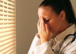 Female doctor with head pain standing near window