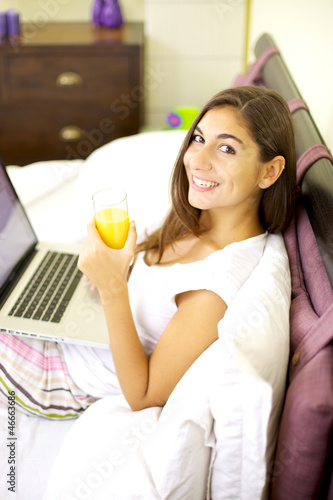 Photo: Happy woman smiling working in bed with computer Happy woman smiling working in bed with computer