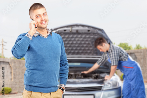 Photo: Smiling guy talking on a phone while in the background mechanic Smiling guy talking on a phone while in the background mechanic
