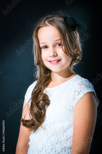 Photo: cute girl in white lacy dress and black hat on dark background cute girl in white lacy dress and black hat on dark background