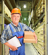 Male worker in uniform holding boxes and clipboard at warehouse