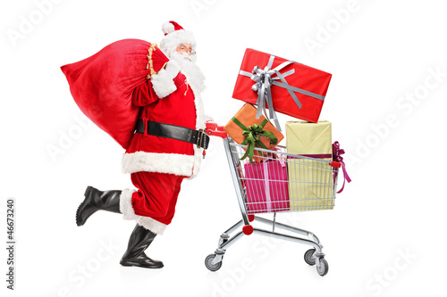 Photo: Santa Claus carrying a bag and pushing a shopping cart full of g Santa Claus carrying a bag and pushing a shopping cart full of g