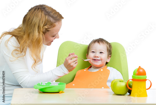 Photo: young mother spoon feeding her baby boy isolated on white young mother spoon feeding her baby boy isolated on white