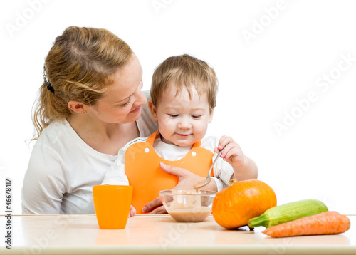 Photo: young mother spoon feeding her baby boy isolated on white young mother spoon feeding her baby boy isolated on white