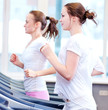 Photo: Two young sporty women run on machine Two young sporty women run on machine