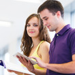Foto : Two college students in library, reading books, using tablet com Two college students in library, reading books, using tablet com