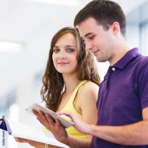 Photo: Two college students in library, reading books, using tablet com Two college students in library, reading books, using tablet com