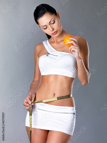 Photo: Girl measures figure with a measuring tape and holding orange Girl measures figure with a measuring tape and holding orange