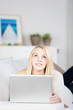 blonde frau liegt mit laptop auf dem sofa