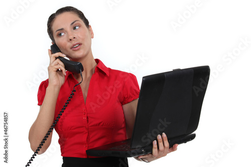 Photo: Secretary holding a laptop while talking on the phone Secretary holding a laptop while talking on the phone