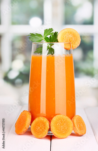 Photo: Glass of carrot juice on wooden table, on window background Glass of carrot juice on wooden table, on window background