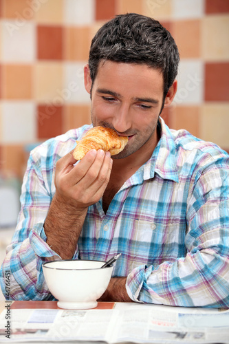 Photo: Smiling man eating croissant for breakfast with a magazine Smiling man eating croissant for breakfast with a magazine