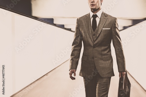 Photo: Man in classic suit with briefcase walking through corridor Man in classic suit with briefcase walking through corridor