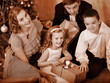 Family with children  receiving gifts under Christmas tree.