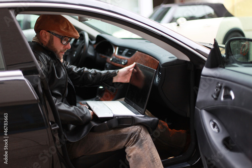Photo: Mann sitzt im Auto mit Laptop Mann sitzt im Auto mit Laptop