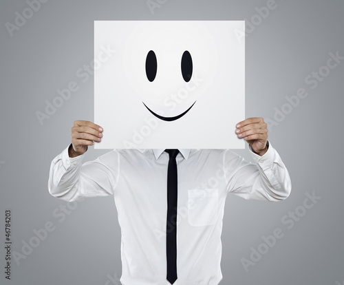 Photo: Young businessman holding card with a happy face on it Young businessman holding card with a happy face on it