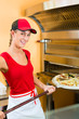 Photo: Frau schiebt die Pizza in den Ofen Frau schiebt die Pizza in den Ofen