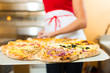 Frau schiebt die Pizza in den Ofen