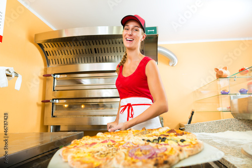 Photo: Frau schiebt die Pizza in den Ofen Frau schiebt die Pizza in den Ofen