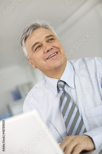 Photo: Portrait of senior businessman in office working on laptop Portrait of senior businessman in office working on laptop
