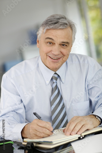 Photo: Portrait of senior businessman writing on agenda Portrait of senior businessman writing on agenda