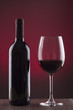 Botella de vino y copa sobre fondo rojo