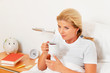 Frau im Bett ist Krank und hat Fieberthermometer.