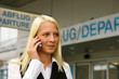Blondes Mädchen telefoniert am Flughafen mit dem H