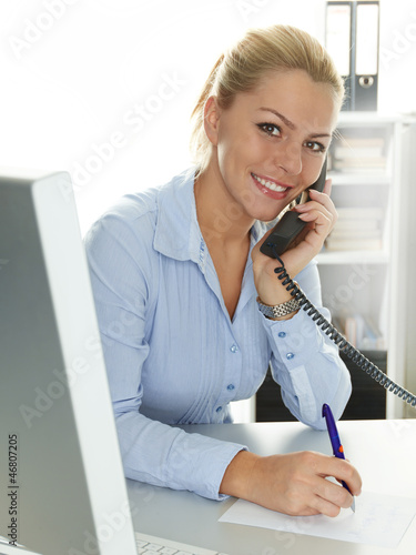 Photo: Female office assistant has a call and makes notes at the office Female office assistant has a call and makes notes at the office