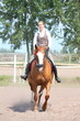 Beautiful young blonde woman riding chestnut horse