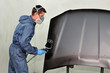 Worker painting car parts in black.