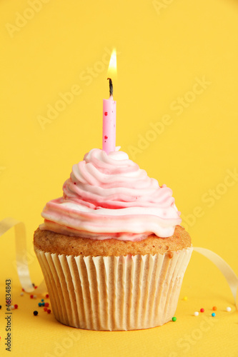 Photo: tasty birthday cupcake with candle, on yellow background tasty birthday cupcake with candle, on yellow background