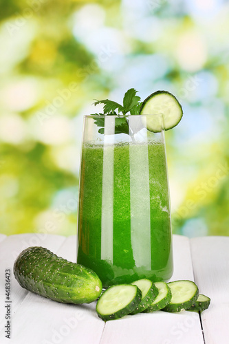Photo: Glass of cucumber juice on wooden table, on green background Glass of cucumber juice on wooden table, on green background