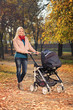 Mother pushing a baby stroller in a park in autumn