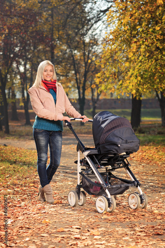 Photo: Mother pushing a baby stroller in a park in autumn Mother pushing a baby stroller in a park in autumn