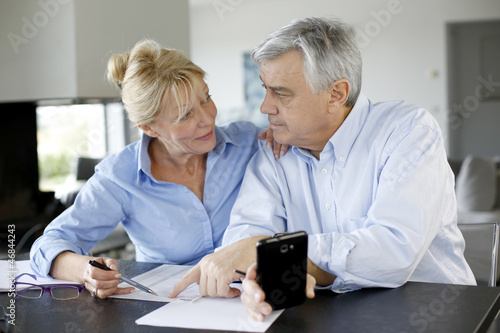 Photo: Senior couple calculting bills amount using smartphone Senior couple calculting bills amount using smartphone