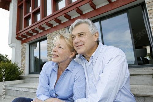 Photo: Senior couple sitting in front of house and looking away Senior couple sitting in front of house and looking away