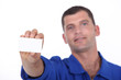 Man in blue overalls holding up a blank business card