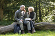 A mature couple sitting on a tree trunk eating a packed lunch