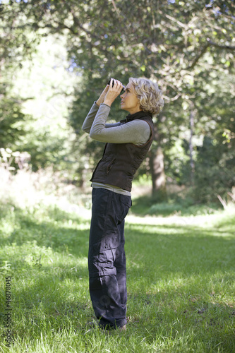 Photo: A mature woman outdoors, looking through a pair of binoculars A mature woman outdoors, looking through a pair of binoculars